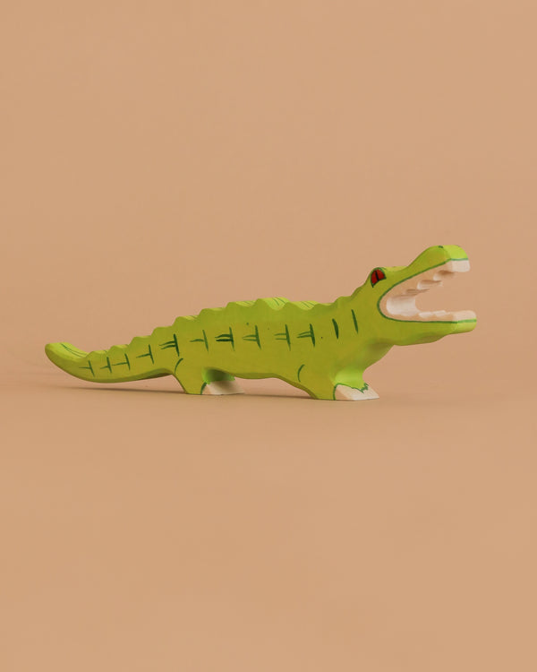 The Holztiger Crocodile is a small, hand-carved green wooden figurine with painted details and an open mouth, crafted in Europe and shown against a plain beige background.