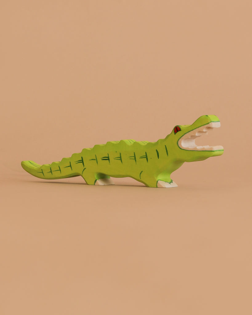 The Holztiger Crocodile is a small, hand-carved green wooden figurine with painted details and an open mouth, crafted in Europe and shown against a plain beige background.