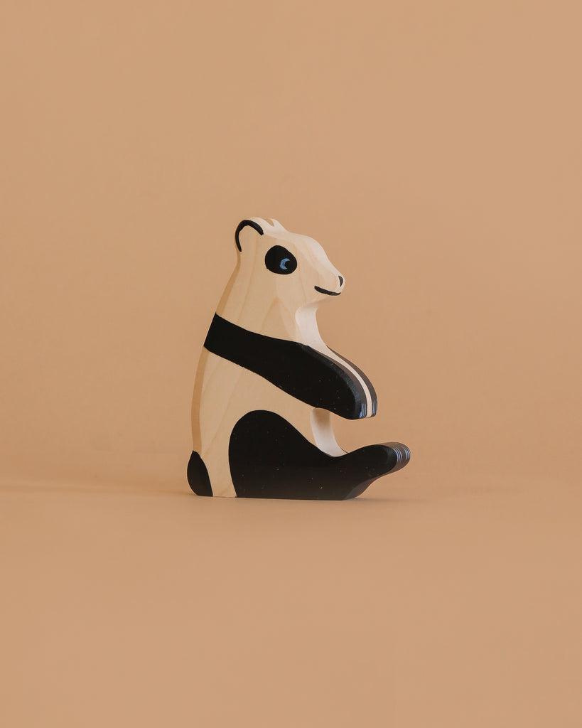 The Holztiger Panda Bear, Sitting is a handcrafted wooden figurine with a minimalist design, painted in black and white. It sits on a beige surface against a matching background, showcasing the charm of European-made wood toys.