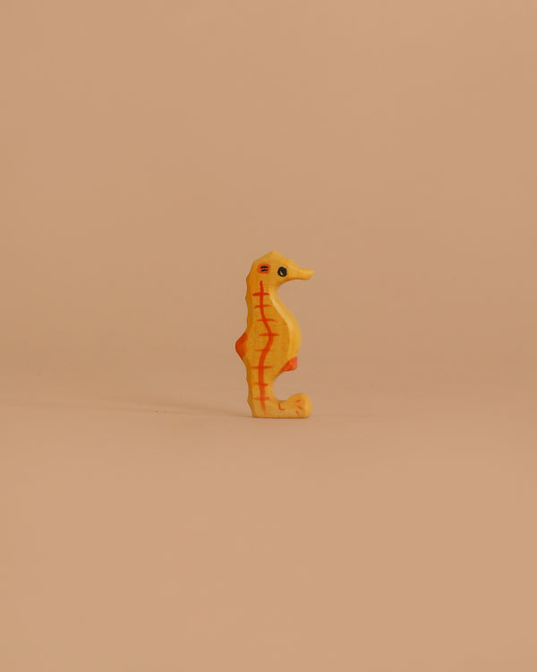 The Holztiger Seahorse is a small, yellow-orange wooden toy with red markings, standing upright on a light beige background—a charming handcrafted figure made in Europe.