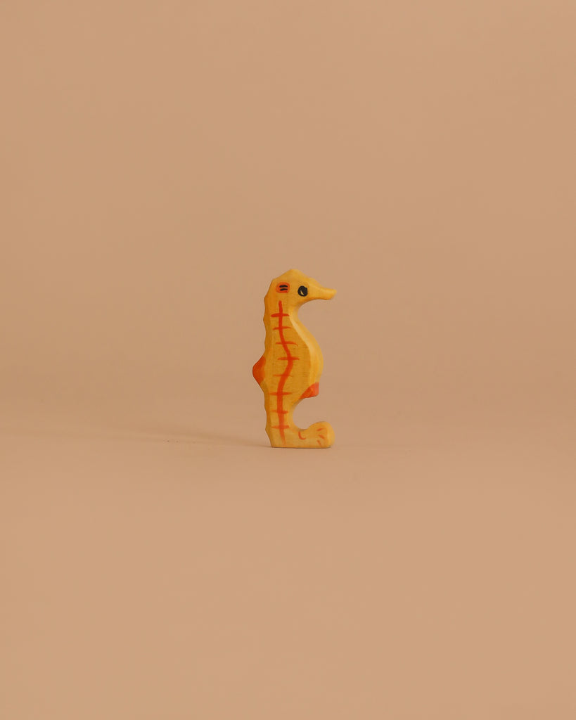 The Holztiger Seahorse is a small, yellow-orange wooden toy with red markings, standing upright on a light beige background—a charming handcrafted figure made in Europe.