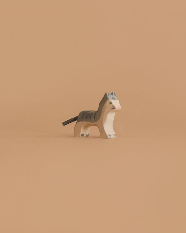 The Holztiger Cat, Small is a wooden figurine with painted gray stripes, green eyes, and a brown tail, shown standing on a plain beige background.
