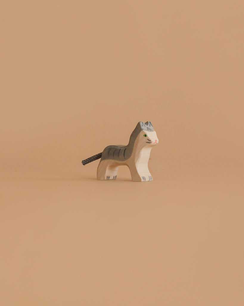 The Holztiger Cat, Small is a wooden figurine with painted gray stripes, green eyes, and a brown tail, shown standing on a plain beige background.