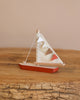 The Handmade Small Wooden Boat, crafted from beech with a cream fabric sail and orange, white, and brown triangular flags, features a hull painted in non-toxic orange. It sits on a wooden surface against a beige background and is proudly made in Ukraine.