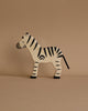 A handcrafted zebra from the Holztiger Handmade Wooden Safari Animals Set, featuring black stripes, stands on a beige surface—ideal for imaginative play and a charming addition to any Holztiger collection.