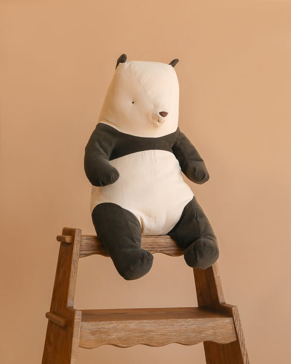 The Maileg Panda Stuffed Animal, Large, with black and white cotton fur, sits atop a wooden ladder against a plain beige background.