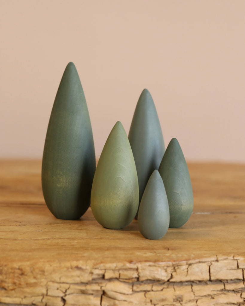 The Handmade Wooden Bush Set features five cone-shaped wooden figures in different sizes and green shades, crafted with non-toxic paint. Arranged on wood against a neutral backdrop, these charming tree-like pieces are proudly made in Ukraine.