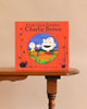 A copy of It’s the Great Pumpkin, Charlie Brown by Charles M. Schulz stands on a wooden table, featuring Peanuts characters and pumpkins on its red cover.