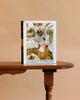 A Bright Days - 1000 Piece Jigsaw Puzzle box featuring a woman in a vibrant, cozy room stands upright on a wooden table with a plain beige background.