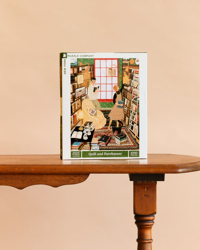 Quill and Parchment - 1000 Piece Jigsaw Puzzle rests on a wooden table, showing an illustrated scene of two people in a cozy bookstore filled with bookshelves and a large window.