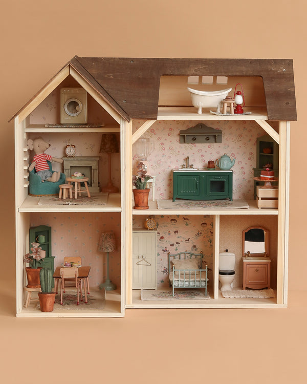 The Maileg Fully Furnished Farmhouse features six detailed rooms with miniature furniture and plants. Patterned wallpaper and a Maileg mouse doll in an armchair create a cozy, inviting dollhouse atmosphere.