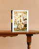Stay Cozy - 1000 Piece Jigsaw Puzzle features animals in a festive room with books, warm lighting, and a window—set on a wooden table, it’s the perfect holiday gift.