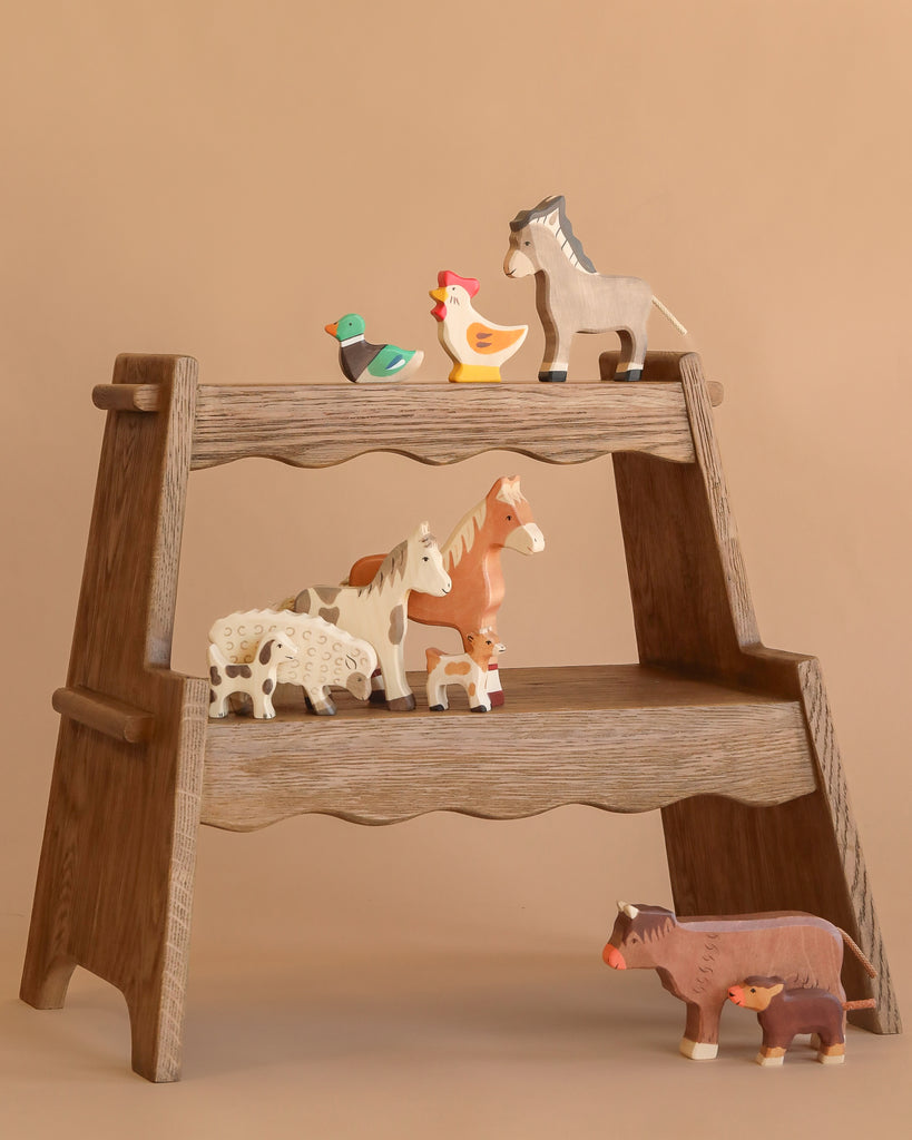 The Holztiger Handmade Wooden Farm Animals Set, crafted from maple and beech wood, features a duck, chicken, donkey, goat, horse, dog, pig, and cow on a wooden display shelf against a plain beige background.