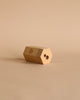 A hexagonal wooden dual pencil sharpener with two holes sits on a beige surface, sporting a small geometric logo—ideal for use with the Moulin Roty Botanist Coloring Book with Stockmar Pencil Set.