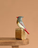 The Hand Carved Ornament - Cardinal Bird- Female - 7"H is a handcrafted wooden figurine in gray, white, and red perched on a block—ideal as an anniversary gift, shown against a plain light brown background.