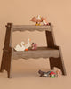 A small wooden display stand with two shelves holds the Holztiger Handmade Wooden Woodland Animals Set, featuring figures like an eagle, owl, swans, and squirrel. More handmade wooden toys and mushroom figures are arranged on the floor below.