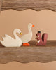 Part of the Holztiger Handmade Wooden Woodland Animals Set, a white swan, a white duck with orange beak and feet, and a brown squirrel made from maple and beech wood stand on a wooden shelf against a beige background.