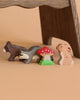 The Holztiger Handmade Wooden Woodland Animals Set features a bear, badger, rabbit, and a red-and-white mushroom displayed in a row on a tan background beneath a wooden surface.