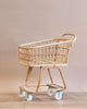 A vintage Rattan Grocery shopping cart with a metal frame and white wheels, standing against a neutral beige background.