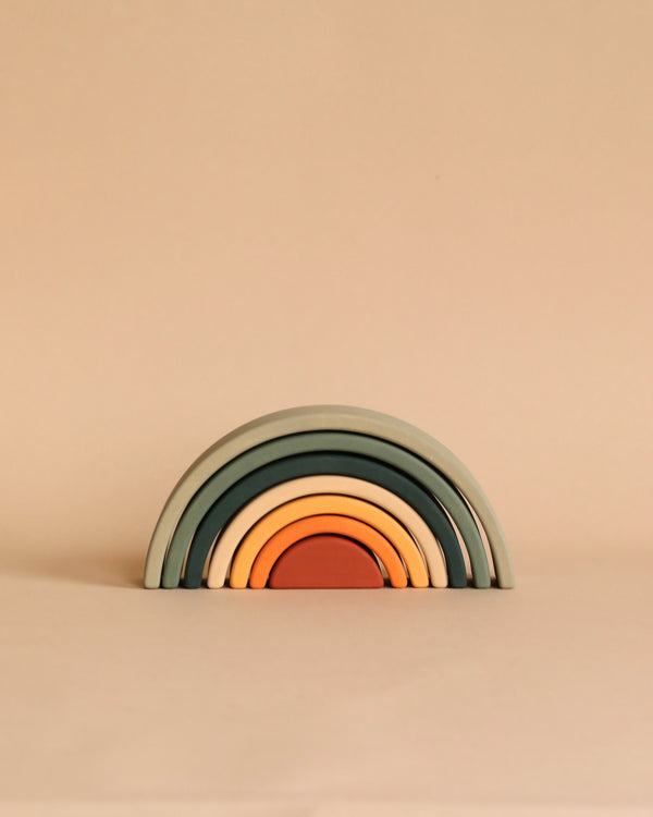 A handmade Mini Rainbow Stacker - Jungle consisting of five arches in earth tones, neatly nested together against a light peach background.