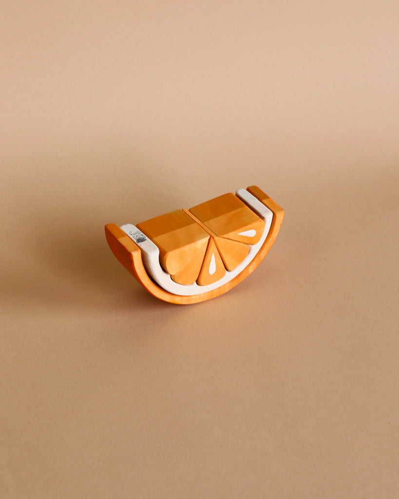 An orange citrus fruit ceramic juicer with a half-slice design, placed on a wooden tangerine stacking toy background.