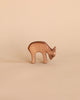 A handcrafted wooden figure of an Ostheimer Deer - Eating, carved with simplistic details and smooth edges, stands against a plain, light beige background.