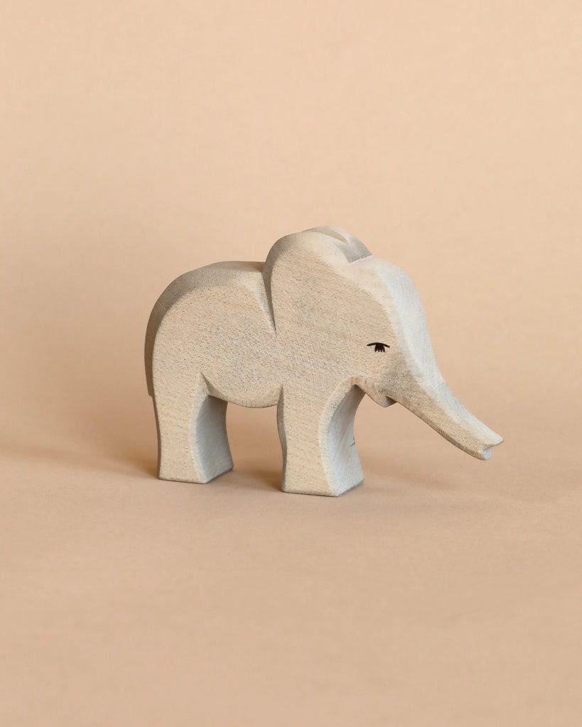 The Ostheimer Handmade Wooden Safari Animals Set features a small, light gray handcrafted wooden elephant with simple carved details, standing on a beige surface—perfect for imaginative play.