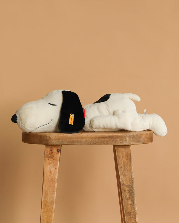The Steiff XL Snoopy Lying Down 16" toy rests on its side atop a wooden stool set against a plain beige background.