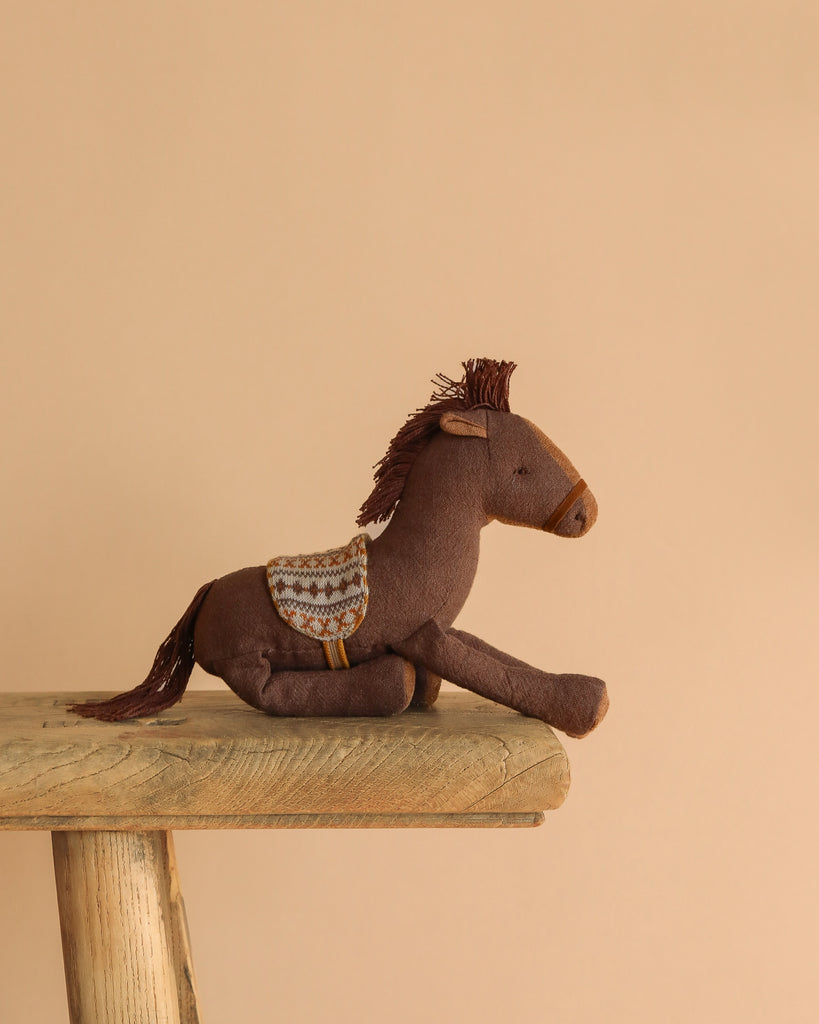 The Easter Basket Gift Set features a brown plush toy horse with a patterned saddle on a rustic wooden bench, perfect for adventures with the Maileg Cowboy Mouse against a plain beige background.