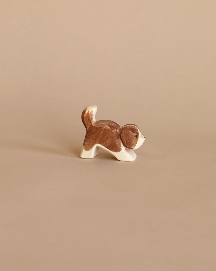 A small, handcrafted figurine of an Ostheimer Small Saint Bernhard Dog - Head Down in a playful stance, isolated against a plain beige background.