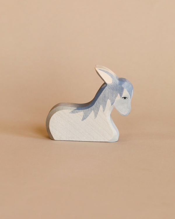 An Ostheimer Donkey - Resting wooden figurine painted in shades of gray and white, displayed against a plain beige background. The donkey is in a resting pose with detailed eyes and ears.