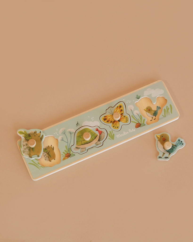 The Moulin Roty Wooden Animal Puzzle - The Three Little Rabbits features four charming animal pieces—a hedgehog, turtle, butterfly, and bird—set against a beige background, ideal as a toddler shape sorter.