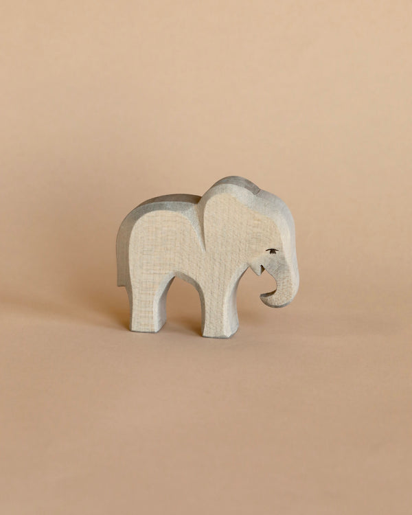 A small Ostheimer elephant figurine stands on a beige background. This handcrafted wooden toy has a simple, smooth design with visible wood grain and a small, painted eye.