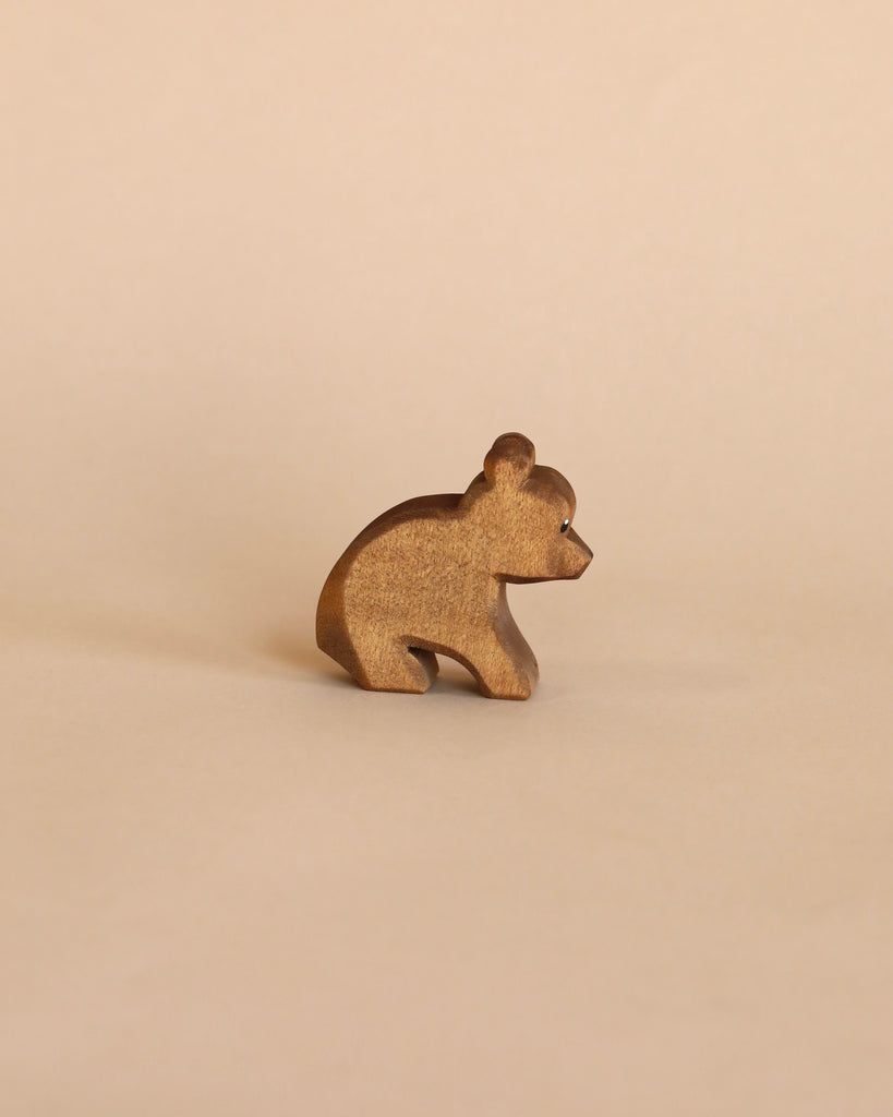 The Ostheimer Handmade Wooden Bear Set features a small, brown, handcrafted wooden bear figurine displayed on a beige surface and background.
