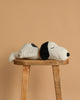 The Steiff XL Snoopy Lying Down 16", featuring black ears and a black spot on its back, is resting on its side atop a wooden stool with a plain beige background.
