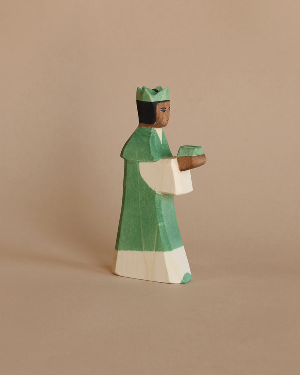 A handcrafted Ostheimer Green King With Crown figurine, wearing a green and white striped outfit and a green hat, holding a book, against a solid light brown background.