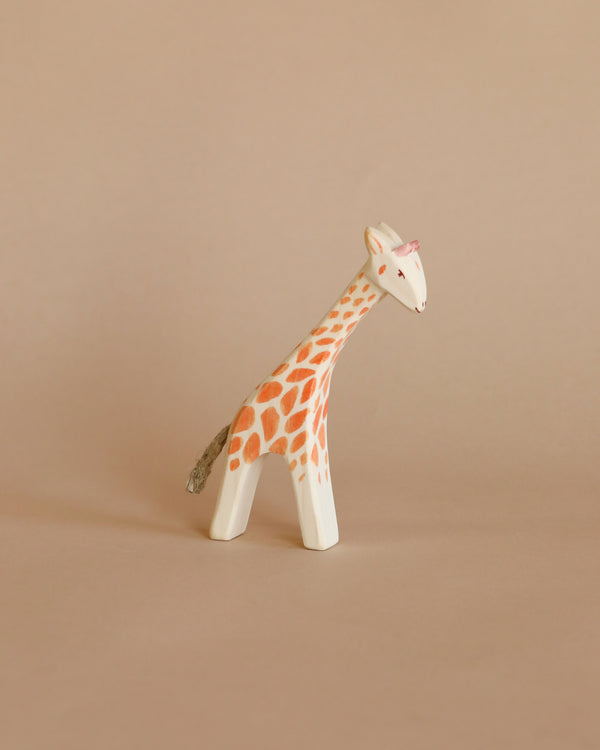 A Ostheimer Small Giraffe - Head Low figurine with orange spots and a glossy finish stands against a plain beige background.