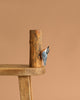 The Hand Carved Ornament - Red Breasted Nuthatch Bird- 8"H is shown clinging to a sustainable softwood tree log, displayed on a wooden table with a plain brown background.