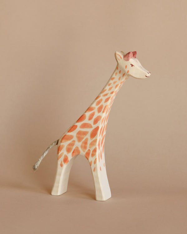 A handcrafted Ostheimer Giraffe - Running figurine painted with orange spots and details, standing against a soft beige background.
