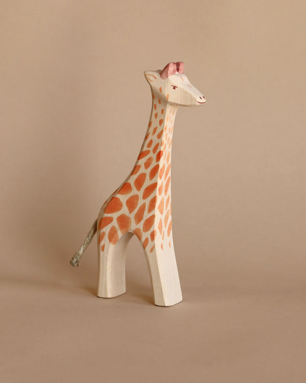 A Ostheimer Giraffe - Standing with hand-painted orange spots and a detailed face stands against a plain beige background.