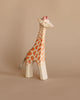 The Ostheimer Handmade Wooden Safari Animals Set features a handcrafted wooden giraffe with orange spots and a pink detail on its head, standing against a beige background—perfect for imaginative play.