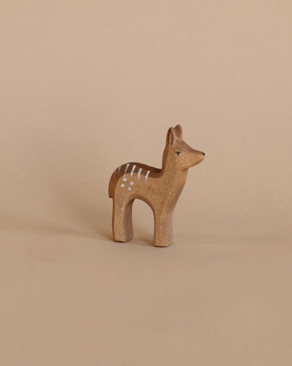 A small, handcrafted Ostheimer Red Deer - Fawn Standing with painted white stripes on its back, positioned against a plain beige background.