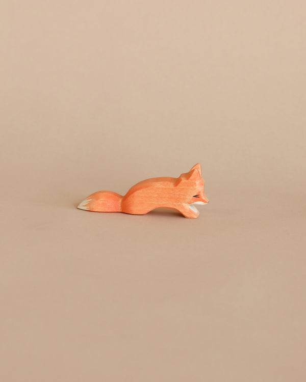 A small, handcrafted Ostheimer Small Fox - Creeping figurine lies on a plain beige background, depicted in a sleek and minimalist design with smooth contours and a subtle orange hue.
