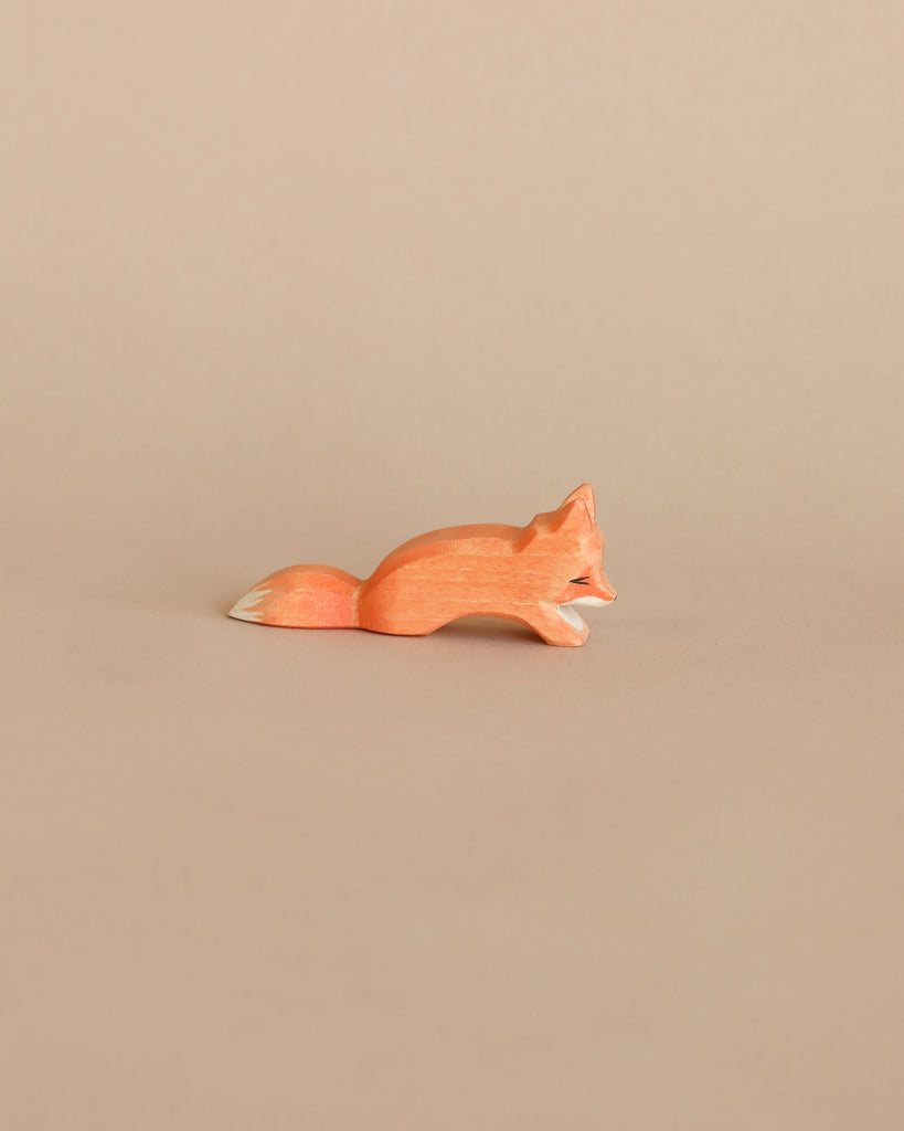 A small, handcrafted Ostheimer Small Fox - Creeping figurine lies on a plain beige background, depicted in a sleek and minimalist design with smooth contours and a subtle orange hue.