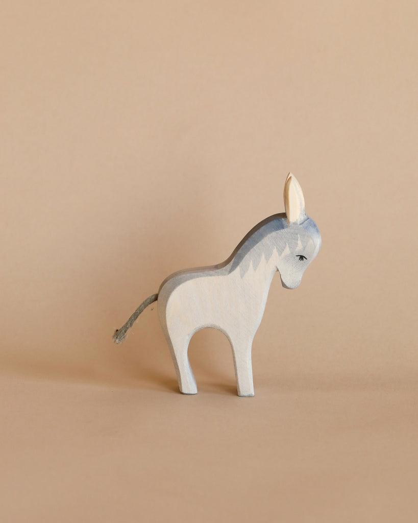 A light grey and white donkey from the Ostheimer Handmade Wooden Farm Animals Set stands on a beige surface with a matching background.