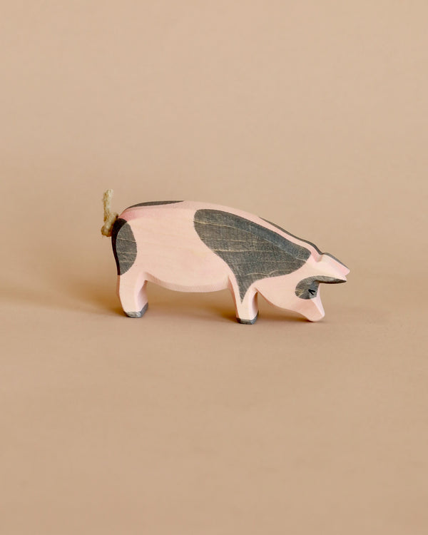 A handcrafted Ostheimer Spotted Pig - Head Low figurine with a simple, stylized design, featuring a pale pink body and gray accents, displayed against a soft beige background.