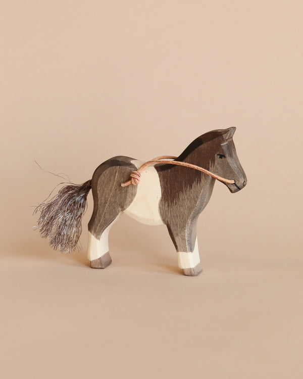 An Ostheimer Pony with a dark brown body, white patches, and a fluffy tail, stands against a soft beige background.