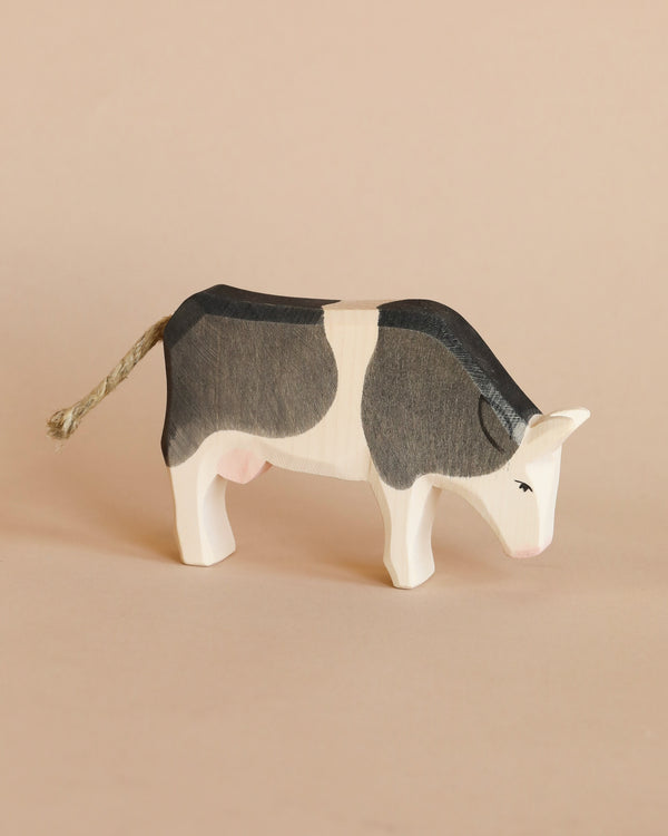 A handcrafted Ostheimer Cow - Black & White - Eating with a black and white pattern, standing on a light beige background. The cow features a textured tail and a small painted eye.