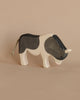 A handcrafted Ostheimer Ox - Black & White toy with a black and white pattern, standing against a plain beige background. The cow has a simplistic design with visible wood grains and a small tail.