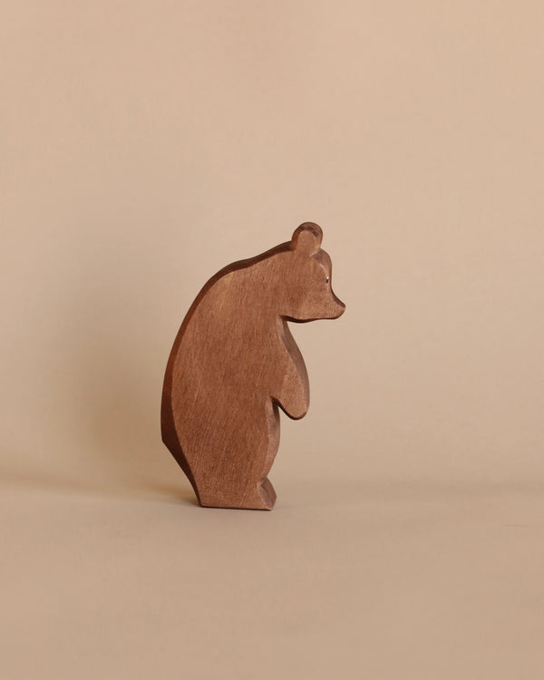 A simple Ostheimer Large Bear - Standing Head Low figurine, an example of handcrafted wooden toys, stands against a plain light beige background, its silhouette showing a side profile with a smooth and stylized shape.